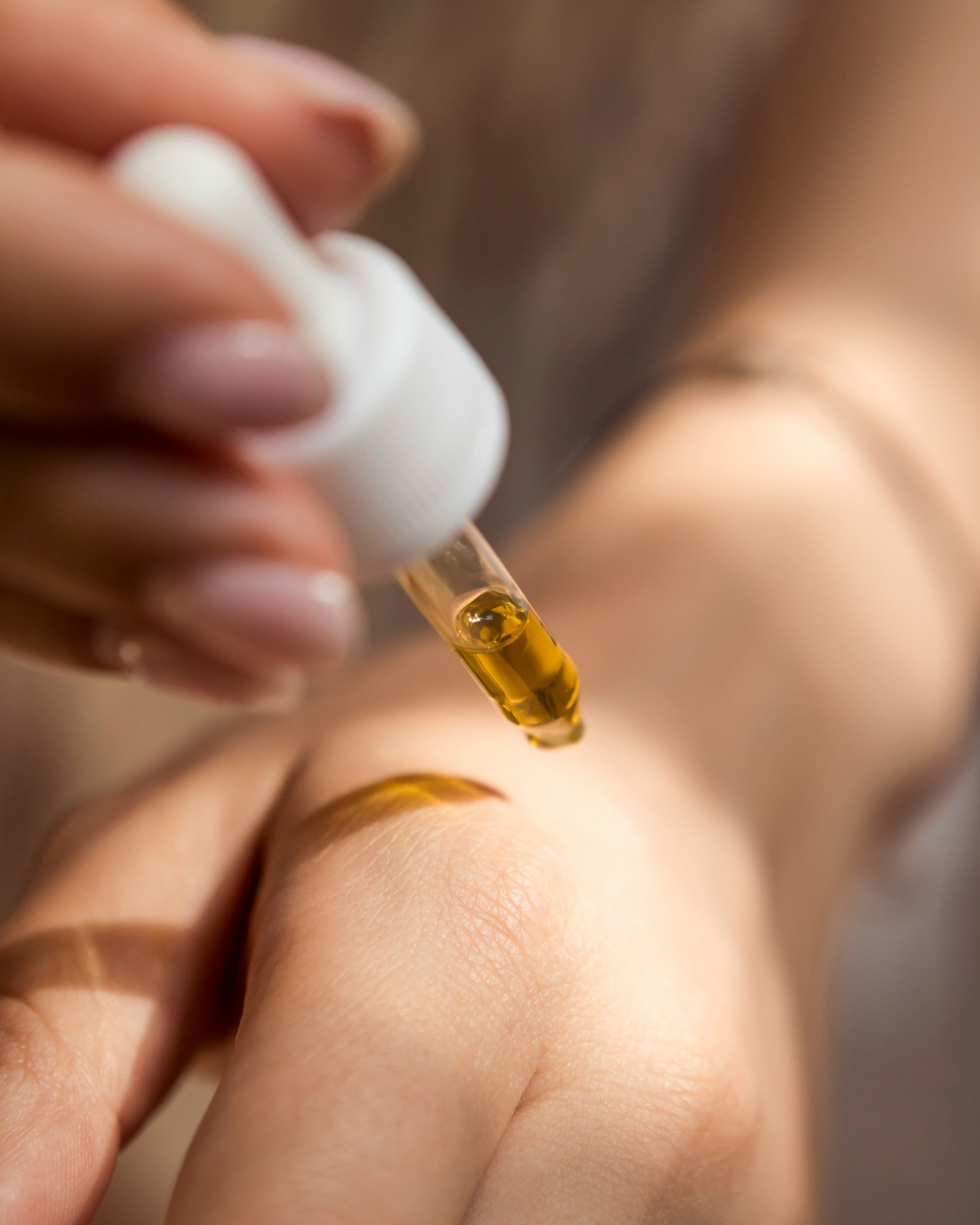Hand with dropper applying golden oil onto another hand.